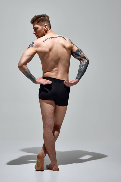 İç çamaşırlı bir adamın arka planda el ele tutuşup kaslı omurgasını gri stüdyo arka planında gösteren dikiz görüntüsü. Uzayı kopyala Doğal güzellik, moda ve tarz kavramı, erkek sağlığı. Ad - Fotoğraf, Görsel