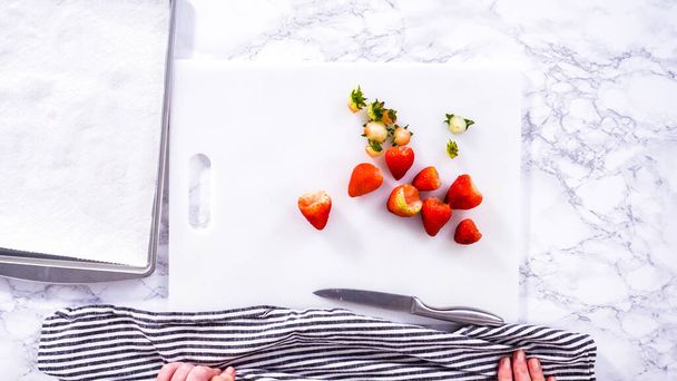 Flat lay. Succulent red strawberries, some showing early spoilage, are arrayed on a white cutting board, held securely in place, with a paper towel lined glass bowl nearby suggesting an attempt at - Photo, Image