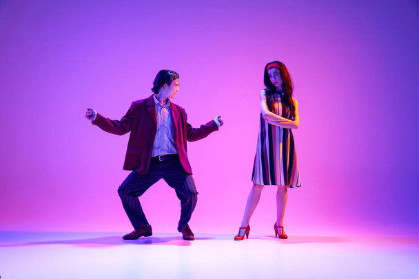 Young man and woman, stylish couple dancing retro dance, boogie woogie against purple background in neon light. Performance. Concept of hobby, dance class, party, 50s, 60s culture, youth - Foto, Imagen