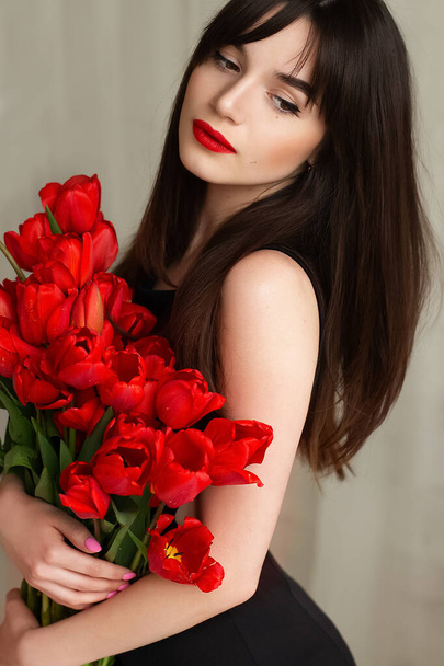 Szczęśliwa atrakcyjna młoda kobieta z kwiatami. Piękna brunetka z bukietem tulipanów. Piękna zmysłowa kobieta trzymająca tulipany. - Zdjęcie, obraz
