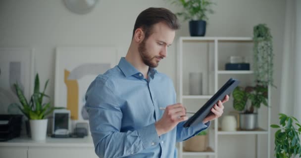Lockdown shot of confident handsome young businessman writing strategy on digital tablet with stylus while standing at corporate workplace - Séquence, vidéo