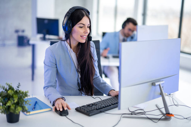 Una joven empresaria sentada en su escritorio, usando auriculares y PC de escritorio para trabajar en la oficina corporativa - Foto, Imagen
