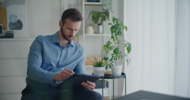 Knappe bebaarde jonge zakenman schrijven strategie op digitale tablet met stylus terwijl zitten op corporate werkruimte - Video