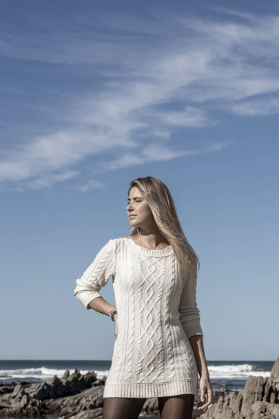 mujer está de pie en una playa con un vestido blanco. El cielo es azul y hay nubes en el fondo - Foto, imagen