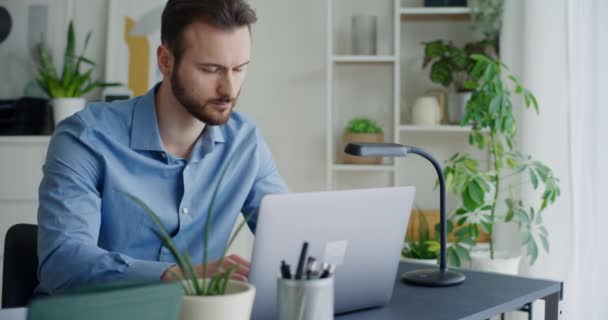 Όμορφος νέος επιχειρηματίας που χρησιμοποιεί φορητό υπολογιστή, ενώ πληκτρολογεί στο γραφείο εργασίας στο εταιρικό γραφείο - Πλάνα, βίντεο