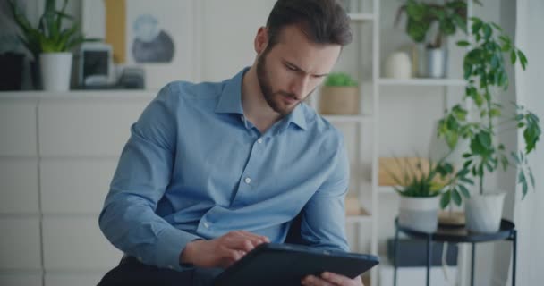 Komea luottavainen nuori liikemies kirjallisesti strategia digitaalinen tabletti stylus istuessaan yrityksen työtila - Materiaali, video