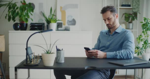 Κλείδωμα πλάνο του νεαρού άνδρα επιχειρηματία γραπτών μηνυμάτων μέσω smartphone, ενώ κάθεται στο γραφείο στο γραφείο - Πλάνα, βίντεο