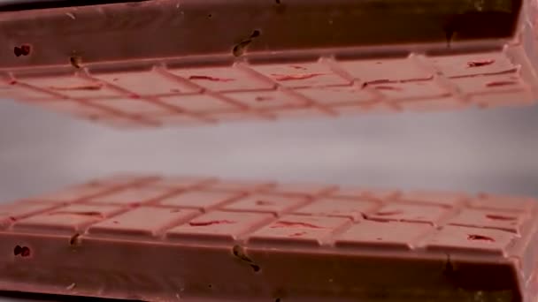 Közelkép a tej rubin csokoládé bár darabok dió mandula és eper, megjelenik a szürke háttér kerül egy fényvisszaverő felületen, így egy tükrözött kép magáról - Felvétel, videó