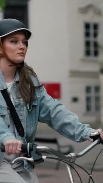 Poważna dziewczyna w kasku jeżdżąca na rowerze po miejskiej ulicy Europy. Uśmiechnięta młoda kobieta styl życia na rowerze w letni środek transportu, ECO przyjazny  - Materiał filmowy, wideo