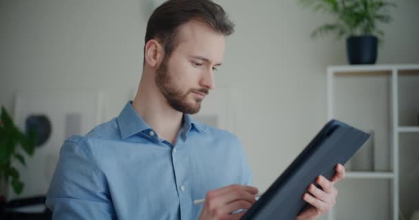 Zelfverzekerde knappe jonge zakenman met behulp van digitale tablet met stylus tijdens het staan in het kantoor - Video