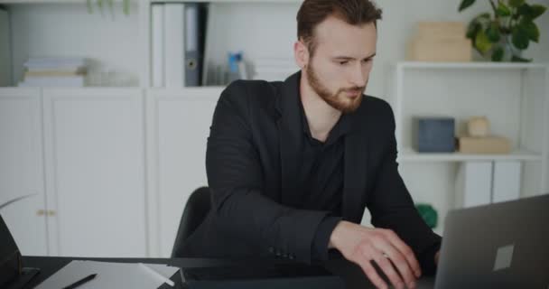 Bezorgde jonge zakenman met behulp van laptop terwijl zitten met hoofd in handen op kantoor bureau - Video