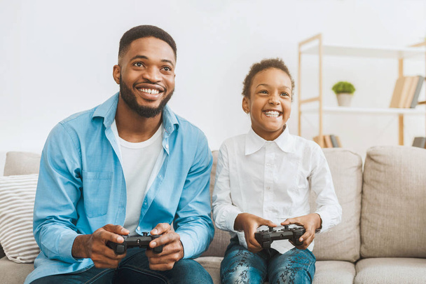 Mutlu afro babalar şirin kızıyla video oyunu oynuyorlar, evde joysticklerle oynuyorlar, bedava yer var. - Fotoğraf, Görsel