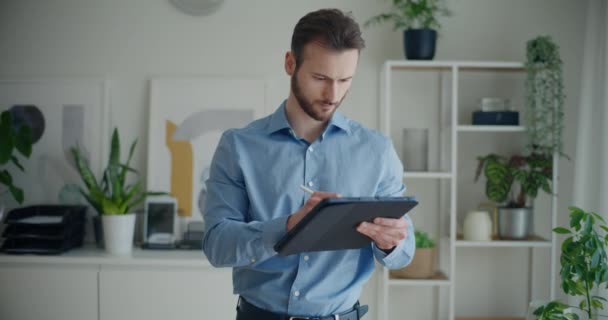 Заблокувати знімок впевненого красивого молодого бізнесмена, який пише стратегію на цифровому планшеті зі стилусом, стоячи в корпоративному офісі - Кадри, відео