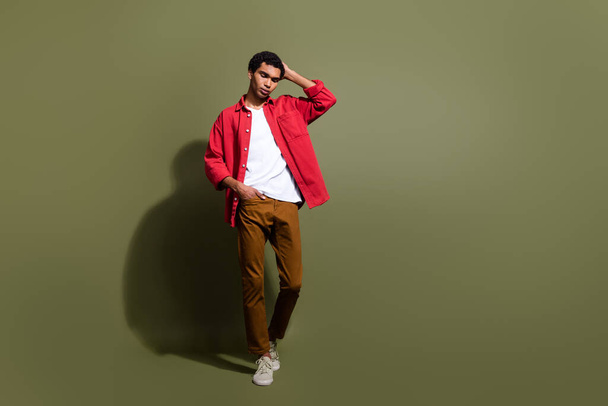 Full length photo of good mood cool man dressed red shirt walking empty space isolated green color background. - Photo, image
