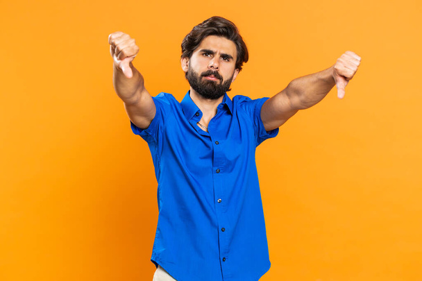 Dislike. Upset unhappy young man showing thumbs down sign gesture, expressing discontent, disapproval, dissatisfied, dislike. Handsome middle eastern guy. Indoors isolated on orange studio background - Photo, Image