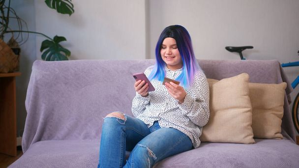 Young latin hispanic teenager girl using credit card and smartphone for online shopping at home. Home interior with plants. Remote shopping, e-commerce, freelance, online shopping, e-shopping concept. - Fotografie, Obrázek