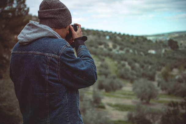Hátsó nézet férfi utazó fotós elfog gyönyörű a hegyek om professzionális digitális fényképezőgép, miközben túrázás és túrázás a kora tavaszi természet. Az emberek és az aktív turizmus fogalma - Fotó, kép