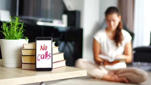 Цифровая фотография концепции детокса. Смартфон с текстом No Calls и женщина читает книгу в фоновом режиме. Высококачественные 4k кадры - Кадры, видео