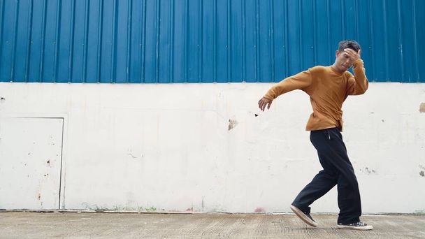 Der hispanische Mann breitet die Arme aus und tanzt vor der Wand. Bewegungsaufnahme eines stilvollen Tänzers oder Choreographen in lässigem Outfit, der im Hip-Hop-Stil tanzt. Outdoor-Sport 2024. Vorfreude. - Foto, Bild