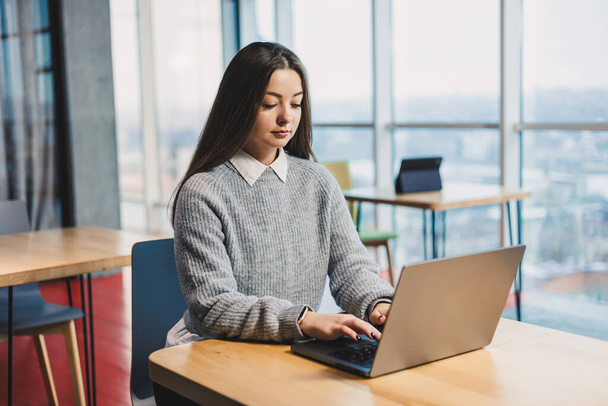 Nette Geschäftsfrau sitzt an einem Schreibtisch in einem modernen Arbeitsbereich und arbeitet an einem Laptop. Arbeitsprozess einer Frau im Büro - Foto, Bild