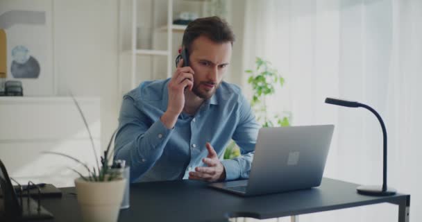 Knappe jonge zakenman bespreken strategie op oproep via mobiele telefoon, terwijl zitten met laptop aan het bureau - Video