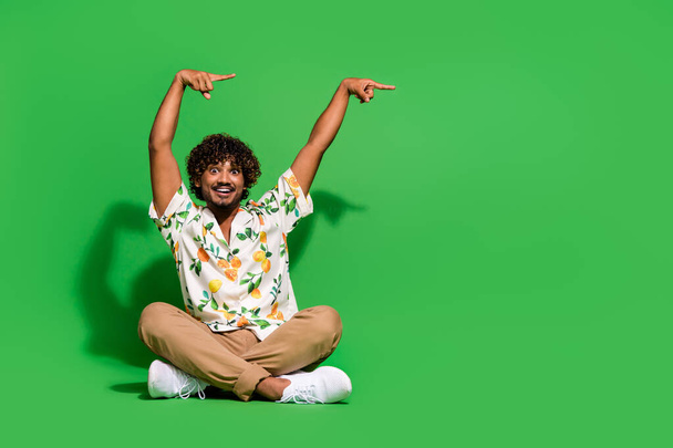 Full size photo of pretty young male sit floor point empty space wear trendy citrus print outfit isolated on green color background. - 写真・画像