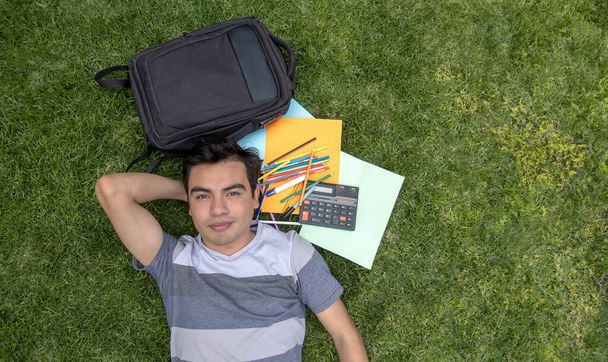 Studente maschio sdraiato sull'erba con uno zaino e una calcolatrice - Foto, immagini