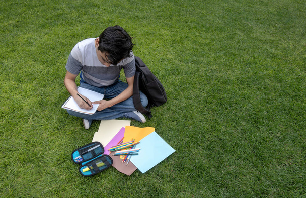 Estudante sentado na grama escrevendo em um caderno - Foto, Imagem