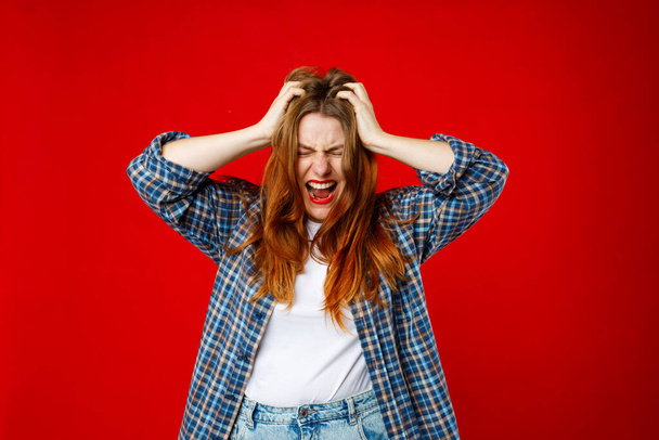 Emocional mujer enojada de 30 años gritando en el fondo rojo del estudio. Cara joven y emocional. Gritando, odio, rabia - Foto, Imagen