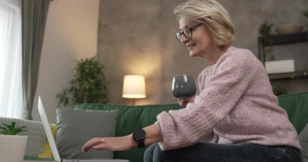 Kypsä blondi valkoihoinen nainen käyttää kannettavaa tietokonetta kotona töihin - Materiaali, video
