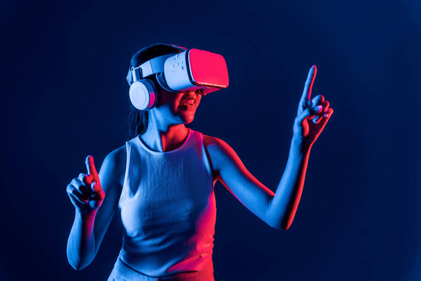 Soporte femenino inteligente con auriculares VR rodeados de luz de neón cyberpunk que conectan tecnología de comunidad ciberespacial metaversa y futurista. Mujer usando el dedo señalando objeto virtual. Alucinaciones. - Foto, imagen