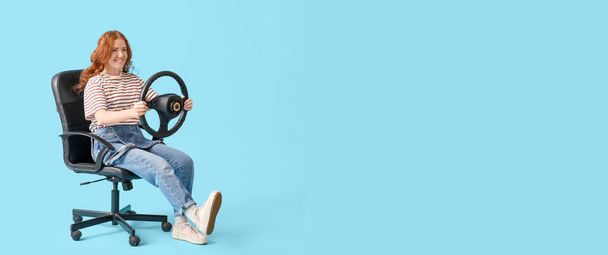 Happy young woman with steering wheel sitting on office chair against blue background with space for text - Photo, Image