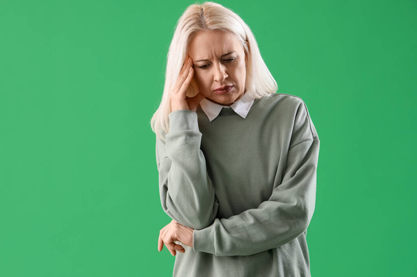 Dojrzała kobieta cierpiąca na ból głowy na zielonym tle - Zdjęcie, obraz