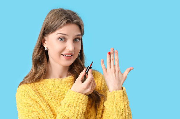 Young woman with nail polish brush on blue background - Photo, Image