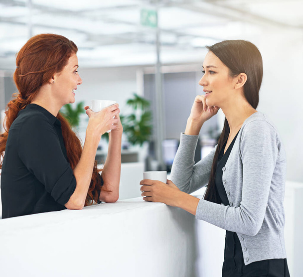 Business women, coffee break and conversation in office with gossip, story and news with partner. Work friends, happy and listening with drink, latte and chat to start morning in corporate workplace. - Photo, Image