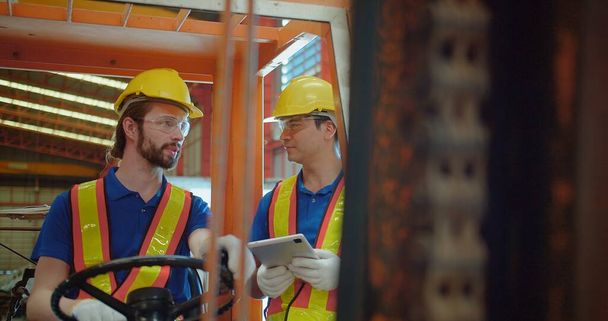 Sárga keménykalapos és biztonsági mellényes építőmunkások építkezési munkagépet üzemeltetnek ipari környezetben, a munkahelyi biztonságra és a csapatmunkára összpontosítanak - Fotó, kép