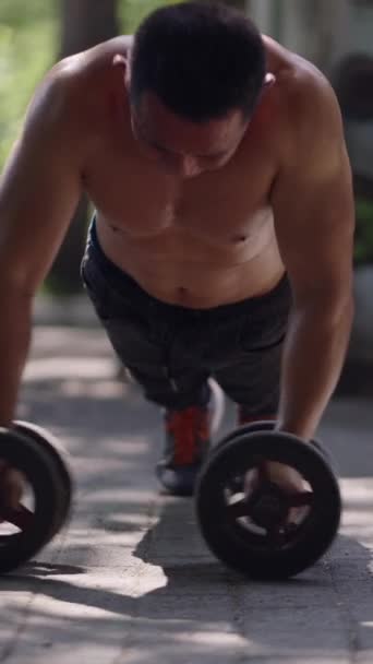 En un gimnasio callejero un hombre hace ejercicio sobre una rueda - FHD Vertical Local street gym - Imágenes, Vídeo