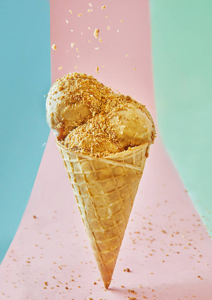 Um cone de sorvete pecan brilhante e tentador com nozes esmagadas em um fundo rosa para um deleite refrescante e delicioso. A imagem é bem iluminada, com cores vibrantes, acrescentando ao seu apelo. - Foto, Imagem
