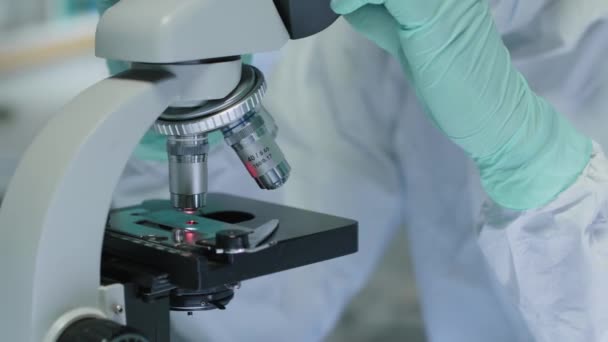 Oříznutý záběr nerozpoznatelného vědce v ochranných pracovních oděvech pomocí mikroskopu při výzkumu v laboratoři - Záběry, video
