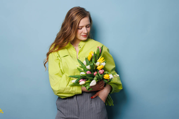 девушка с весенним букетом тюльпанов на чистом голубом фоне, весенние цветы - Фото, изображение