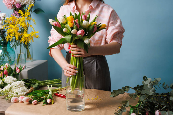 дівчина-флорист збирає букет з весняних квітів тюльпанів на чистому синьому фоні - Фото, зображення