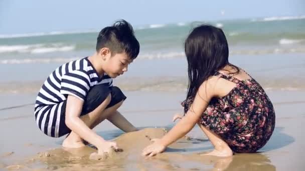 Zbliżenie azjatycki chłopiec i dziewczynka twardy w pracy, budowanie zamków na piasku plaży - Materiał filmowy, wideo