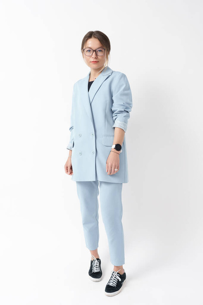 Jonge professionele vrouw in een licht blauw pak en sneakers poseren op witte achtergrond. - Foto, afbeelding