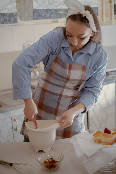 Naispuolinen kondiittori valmistaa kuorrutuksen leivoksille. Nauti kodin leivonnan taiteesta tämän kotitekoisen kondiittorin kanssa herkullisia herkkuja kotona.. - Valokuva, kuva