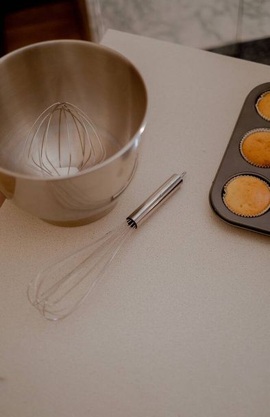 Op de tafel liggen cupcakes, die de artisticiteit van een banketbakker laten zien. De keukentafel toont het gereedschap en de ingrediënten van een banketbakker, klaar voor culinaire creaties. - Foto, afbeelding