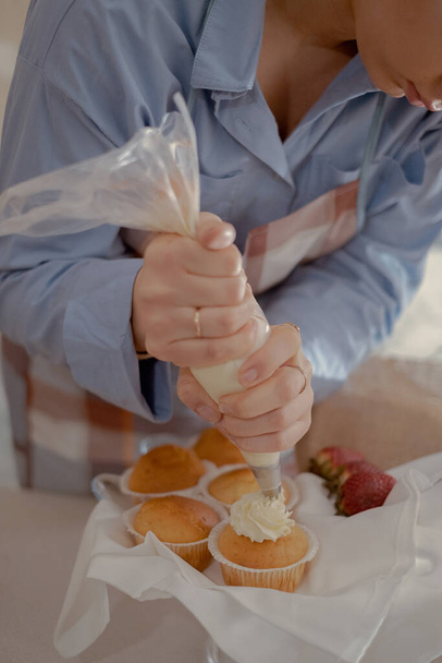Un pasticcere donna tubi glassa su cupcakes, mostrando i suoi prodotti da forno fatti in casa. Esplora il fascino della cucina casalinga e delle piccole imprese con questa immagine di un fornaio esperto al lavoro.. - Foto, immagini