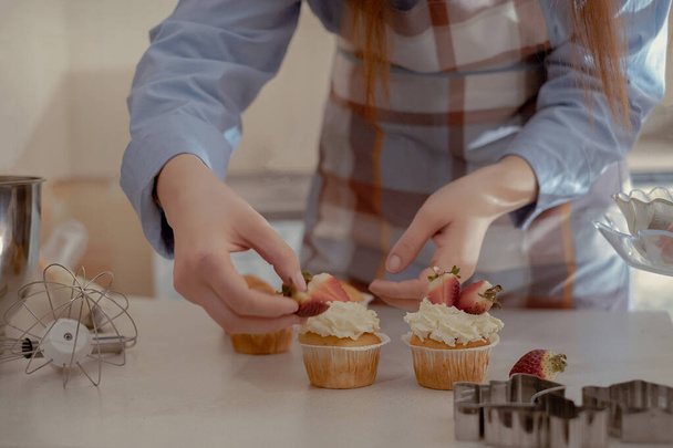 Uma cozinheira de pastelaria feminina decora cupcakes com bagas, exibindo seus produtos caseiros. Explore o charme do cozimento em casa e do negócio em pequena escala com esta imagem de um padeiro qualificado no trabalho. - Foto, Imagem