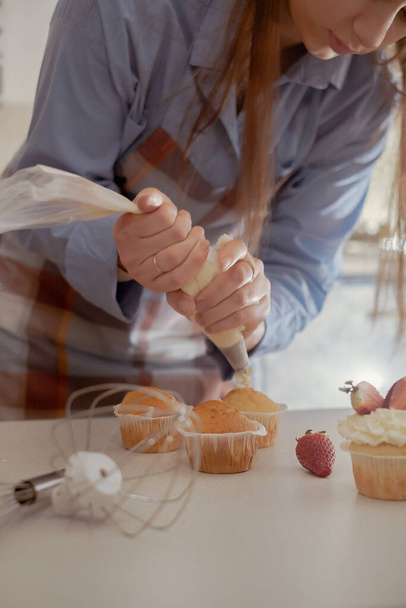 Een vrouwelijke banketbakker versiert cupcakes met bessen en toont haar zelfgebakken producten. Ontdek de charme van thuisbakken en kleinschalig ondernemen met dit imago van een ervaren bakker op het werk. - Foto, afbeelding