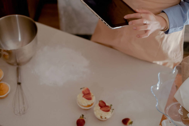 A female pastry chef holds a tablet for managing orders, representing homemade baking. Experience the essence of small-scale, eco-friendly baking with gluten-free and sugar-free products, promoting healthy eating. - Foto, imagen