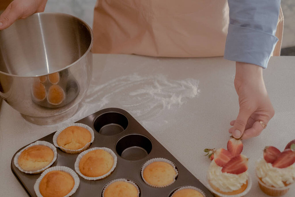 Een vrouwelijke banketbakker versiert cupcakes met bessen en toont haar zelfgebakken producten. Ontdek de charme van thuisbakken en kleinschalig ondernemen met dit imago van een ervaren bakker op het werk. - Foto, afbeelding
